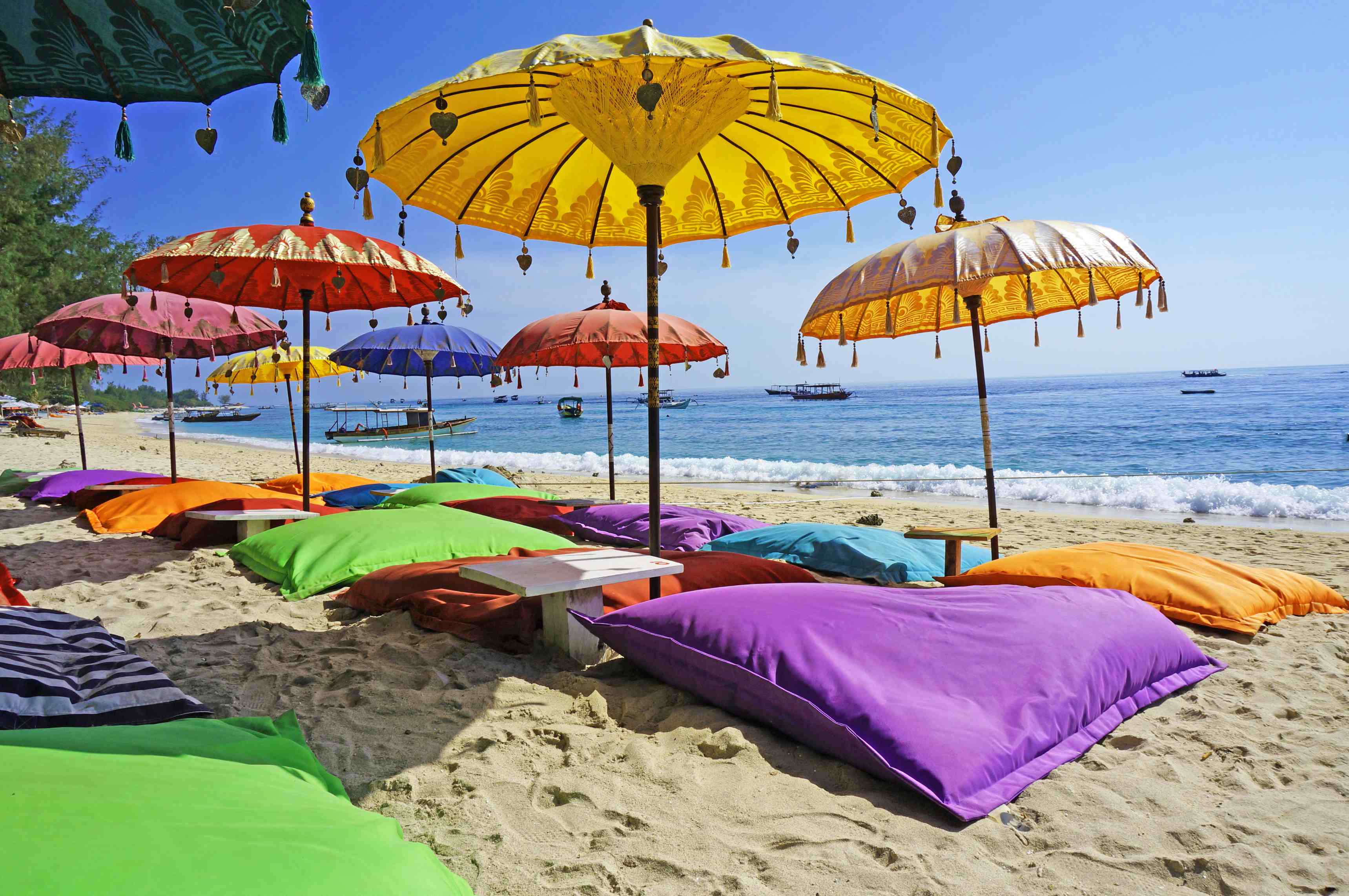 This image shows some colourful beach umbrellas and sand pillows in a pristine tropical beach bathed by the Bali sea.